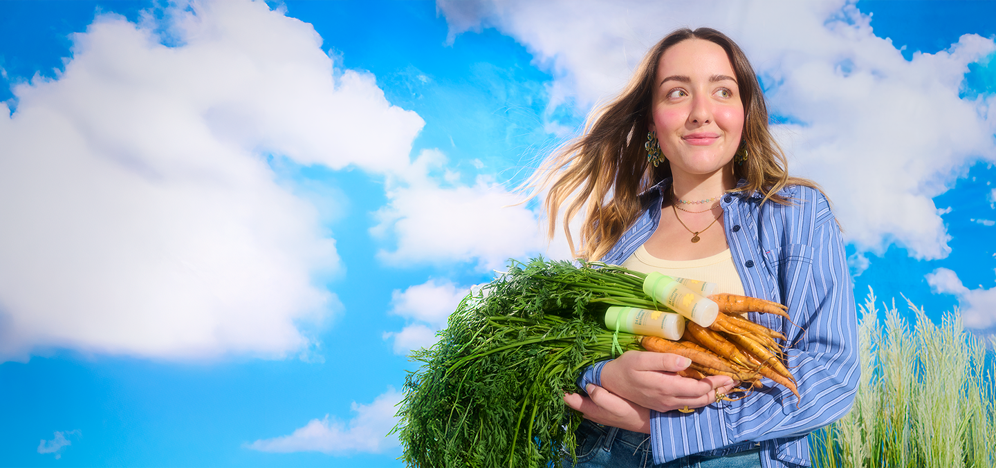 Model holding 24 Carrot Retinal with ugly carrots that provides the upcycled carrot extract for the formula that provides antioxidant benefits