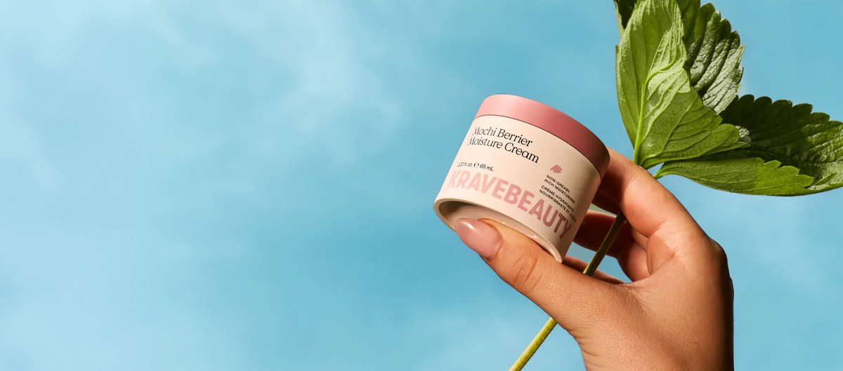A hand holding Mochi Berrier Moisture Cream against a clear blue sky